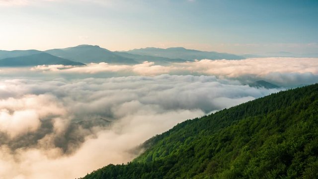 Time lapse with sunrise, low clouds and fast moving morning mists over the tree-covered mountain slopes, the Rhodopes in Bulgaria
