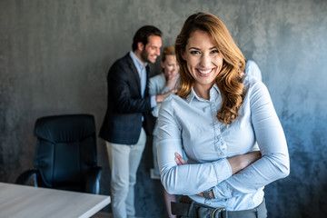Business woman standing in front of their colleagues and looking at the camera with crossed arms