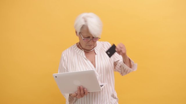 Senior woman trying to insert credit card in the laptop. Online shopping . High quality 4k footage