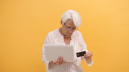 Confused senior woman trying to insert credit card in the laptop. Online shopping . High quality...