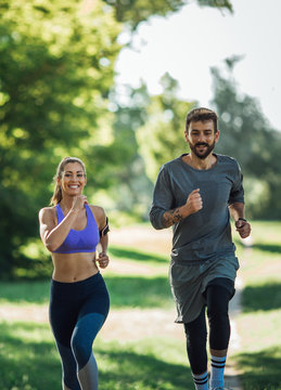 Front image of a young couple jogging in the woods on a sunny day