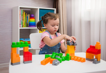 a little girl is playing a multi-colored constructor at a table in the children's room