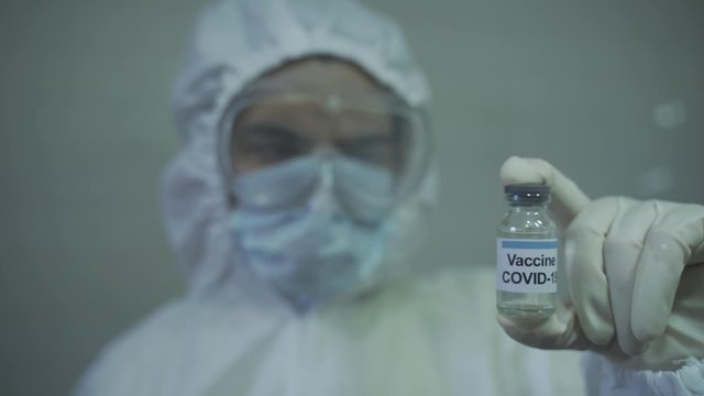 lady doctor wearing protective PPE deep staring at covid 19 vaccine that is in her hand.