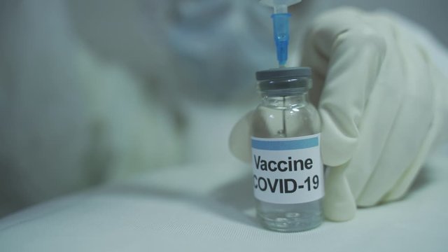 medical worker wearing PPE drawing out covid 19 vaccine from vial. front close up view