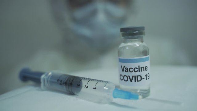 medical worker wearing PPE kit slowly approaching covid vaccine and syringe placed infront of him.
