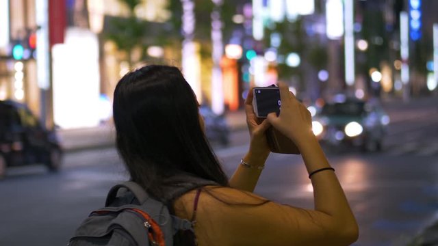 A young female tourist exploring the streets of Tokyo at night in summer taking pictures and photos on her smartphone.