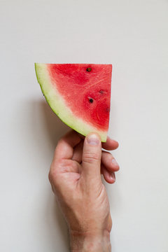 Male hahd holding slice of ripe watermelon on white background, top view