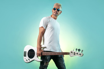 Confident hipster man posing with white bass guitar in neon lights. Rock music concept. Rock star.