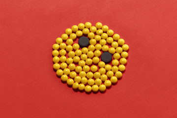 Yellow and black pills lying in the shape of circle, face isolated over red background. Health care and treatment concept.