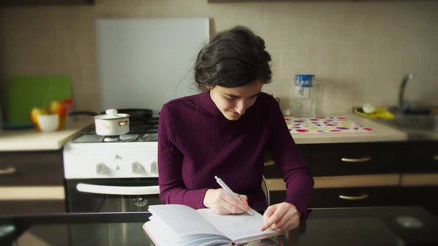 Cute left-handed girl learning to write with her right hand sitting at the table