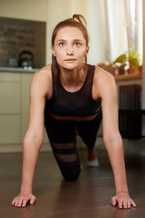 Fototapeta na wymiar A sporty girl in a black workout tight pants and top is relaxing after doing push-ups at home. A woman is practicing exercises for the chest at her apartment.