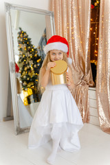 Little cute girl in Santa hat opens a Christmas present.