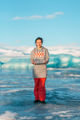 A girl is holding a clean transparent piece of ice in her hands while standing near a glacier in...