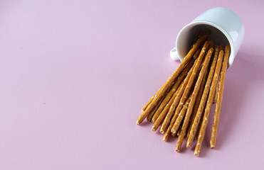 Bread sticks knocked over white cup on the pink background with copy space