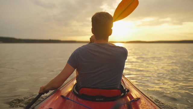 Meeting sunset on kayaks. Rear view of young man kayaking on lake with sunset in the background