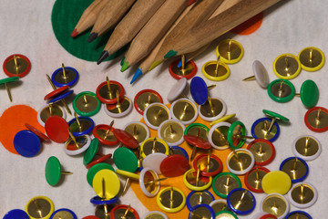 Thumbtacks and colored pencils scattered on a colored plane