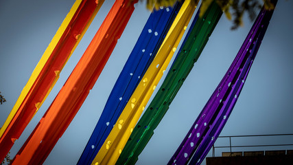 Rainbow gay pride flag against blue sky over building, space for text. LGBT concept