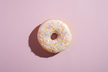 Vanilla donut with sprinkles, sweet glazed dessert food on pink minimal background, top view copy...