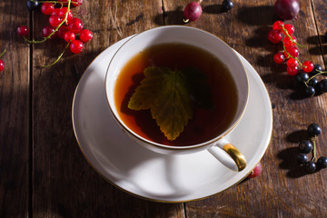 Vintage cup of tea with gold decoration on the old wooden table on which berries lie