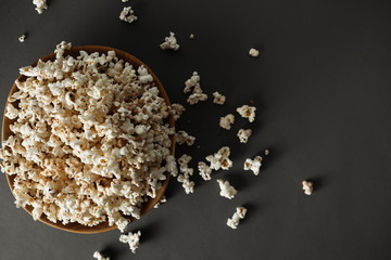 Overhead view of the fresh popcorn in the wooden bowl on the dark grey background