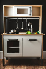 Stylish wooden Scandinavian play kitchen with toy kitchenware and utensils on the black background
