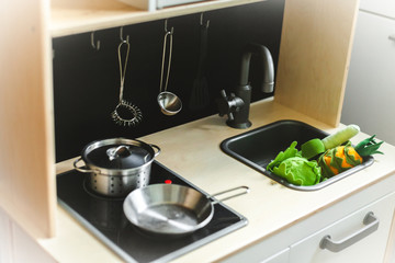 Stylish wooden Scandinavian play kitchen with toy kitchenware and utensils on the black background