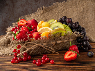 Fresh berries and fruit in a burlap basket on a wooden background. The concept of healthy eating.