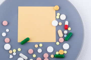Multicolored medical pills, capsules and note paper on a gray ceramic plate. Place for your text.