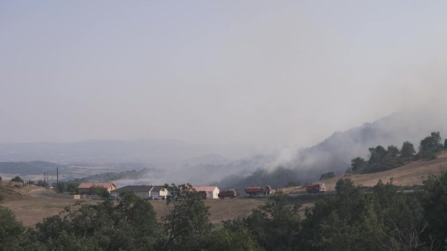 Wide angle view of firefighters overlooking a forest fire with heavy s