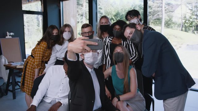 Pandemic lifestyle at work. Happy young multiethnic business people take team selfie photo in COVID-19 masks at office.