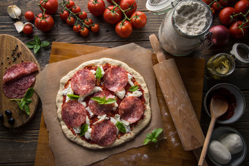 A woman preparing a pizza, knead the dough and puts ingredients on kitchen table.