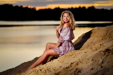 Sitzende blonde Junge Frau mit Locken lächelt am Strand beim Sonnenuntergang.