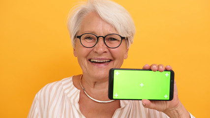 Old woman shoving the smartphone. Green screen for replacement. High quality photo