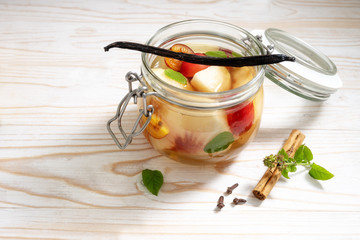 Glass jar with canned fruits flavored with cinnamon, vanilla and mint on a white painted wooden table, copy space
