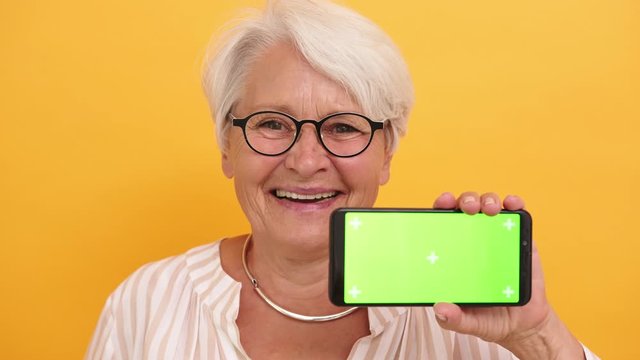 Old smiling woman showing the smartphone. Green screen for replacement. High quality 4k footage