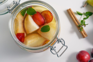 Open glass jar with canned fruits on a white table, high angle view from above, selected focus