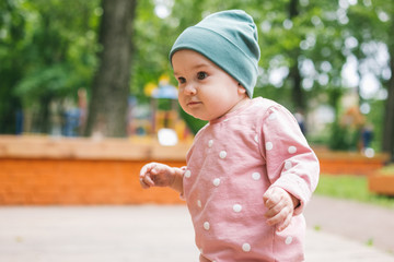 A one-year-old girl in modern stylish children clothing walks on the playground