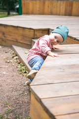 A one-year-old toddler climbs up a step while walking in the playground. Child safety on the street