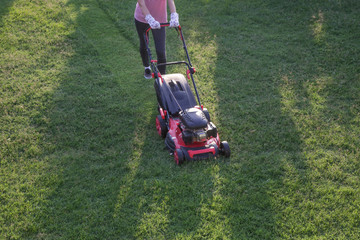 Young woman cutting grass with a lawn mower. Outdoor household chores concept.