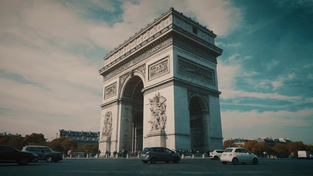 Triumphal arch front view with cars spinning around the roundabout and a cloudy sky