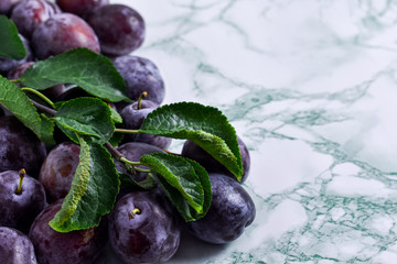 Ripe, juicy plums with a branch and leaves on a green marbled background. Place for your text.