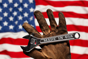 Old worn work glove holding adjustable wrench with Made in USA text. American workforce or...