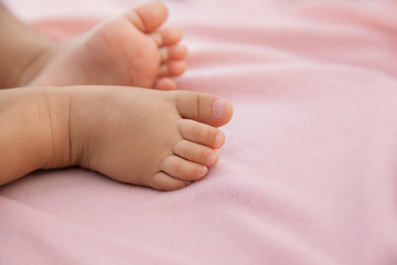 Newborn baby feet on pastel pink background, closeup of infant barefeet in a selective focus
