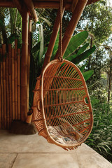 Wicker rattan hanging chair on wooden bamboo terrace in the jungle, nature view. Rattan lounge...