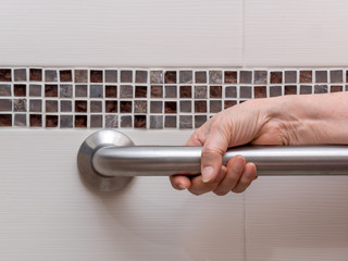 hand of elderly woman holding aluminium rail in toilet. Close up view.