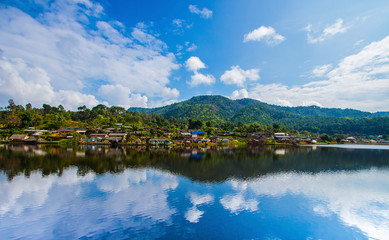 Fototapeta na wymiar The village next to the river. The backdrop has mountains and beautiful blue turquoise sky. The river has a beautiful reflection. Village in Pai, Mae Hong Son, Thailand