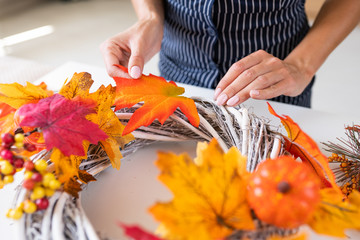 Florist at work: woman makes an autumn wreath at the door from yellow leaves, decorative pumpkins and berries.