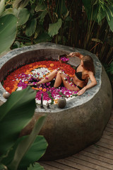 Woman relaxing in round outdoor bath with tropical flowers, organic skin care, luxury spa hotel, lifestyle photo, spa in the jungle