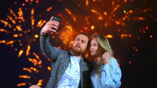 Smile romantic couple make selfie on phone. Colorful fireworks in night sky. Happy smiling man and woman pose front mobile on dating. Loving couple making selfie with firework on phone celebrate date.