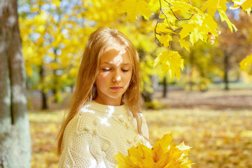 beautiful blonde teen girl walking in an autumn Park with maple trees